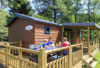 Family enjoying a meal outside a wooden lodge at Cottage in Veluwecamping De Pampel, Netherlands.