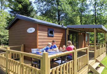 Family enjoying a meal outside a wooden lodge at Cottage in Veluwecamping De Pampel, Netherlands.