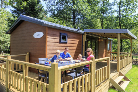 Familia desayunando en la terraza de una cabaña Cottage en Veluwecamping De Pampel, Países Bajos.