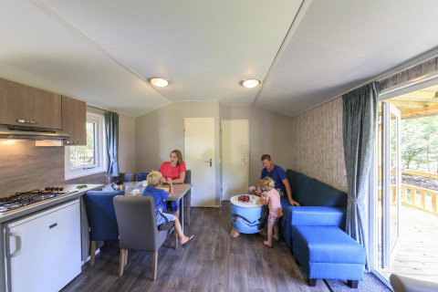 Familie hygger sig indendørs i en hytte på Veluwecamping De Pampel, med køkken og siddeområde.