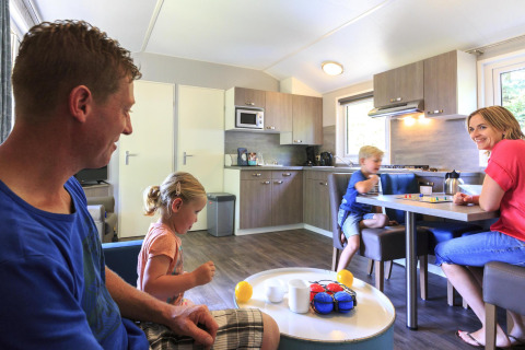 Familia disfrutando en la sala de un Cottage moderno en Veluwecamping De Pampel, Holanda, jugando y charlando.