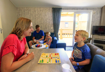 Familie spiller brætspil i stue på Cottage ved Veluwecamping De Pampel, Holland, hyggelig atmosfære.