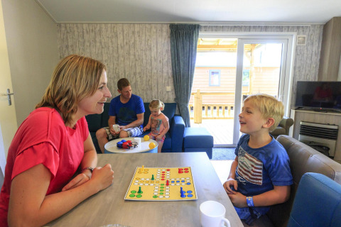 Familia juega a un juego de mesa en la sala del Cottage en Veluwecamping De Pampel, Países Bajos.