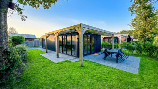 Photo of a modern Eco Lodge at Uniq Leisure in the Netherlands, surrounded by green grass and trees.