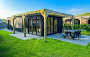 Eco Lodge en Uniq Leisure en Países Bajos, cabaña negra moderna con terraza y césped bajo cielo despejado.