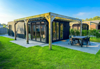 Eco Lodge en Uniq Leisure en Países Bajos, cabaña negra moderna con terraza y césped bajo cielo despejado.