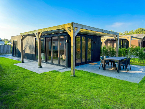 Eco Lodge en Uniq Leisure en Países Bajos, cabaña negra moderna con terraza y césped bajo cielo despejado.