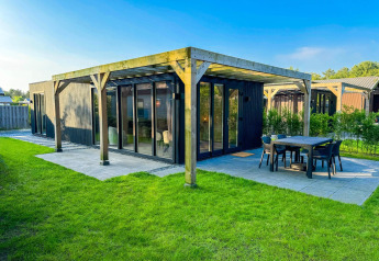 Eco Lodge at Uniq Leisure in the Netherlands, modern black wooden cabin with patio and green lawn, sunny day.