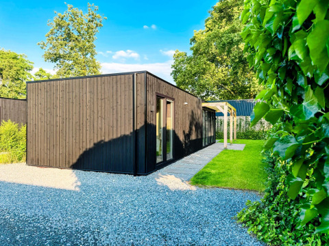 Eco Lodge moderna en Uniq Leisure, Países Bajos, rodeada de jardinería, grava y un cielo azul claro.