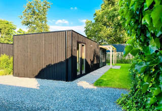Moderne Eco Lodge ved Uniq Leisure i Holland, omgivet af grønt græs og træer under blå himmel.