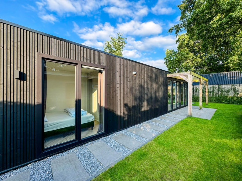 Moderna Eco Lodge en Uniq Leisure, Países Bajos, con fachada de madera negra, grandes ventanas y jardín verde.