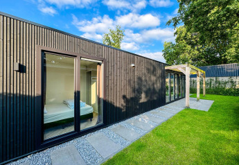 Moderna Eco Lodge en Uniq Leisure, Países Bajos, con fachada de madera negra, grandes ventanas y jardín verde.