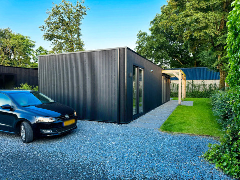 Lodge ecológico moderno y negro en Uniq Leisure, Países Bajos, con estacionamiento y jardín verde.