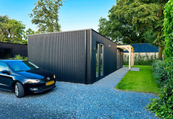 Lodge ecológico moderno y negro en Uniq Leisure, Países Bajos, con estacionamiento y jardín verde.