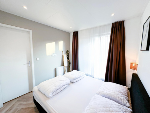 Dormitorio moderno y luminoso en Eco Lodge de Uniq Leisure en los Países Bajos, con cama doble y cortinas oscuras.