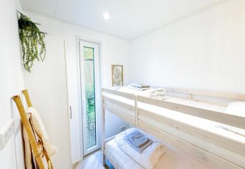 Dormitorio luminoso con litera, planta verde y ventana alta en Eco Lodge de Uniq Leisure en Países Bajos.