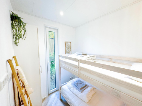 Dormitorio luminoso con litera, planta verde y ventana alta en Eco Lodge de Uniq Leisure en Países Bajos.