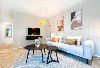 Sala de estar moderna en Eco Lodge en Uniq Leisure, Países Bajos, con sofá claro, arte y televisor en pared.