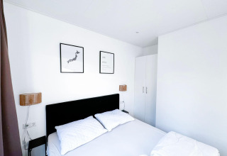 Dormitorio moderno y blanco en Eco Lodge en Uniq Leisure, Países Bajos, con dos cuadros en la pared sobre la cama.