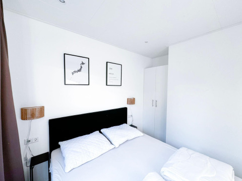 Moderne, hvid soveværelse på Eco Lodge ved Uniq Leisure i Holland med to billeder over en dobbeltseng.