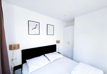 Modern white bedroom at Eco Lodge at Uniq Leisure in the Netherlands, featuring two framed artworks above bed.