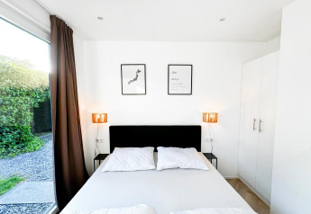 Dormitorio moderno y luminoso en Eco Lodge, Uniq Leisure, Países Bajos, con cama doble y ventanal al jardín.