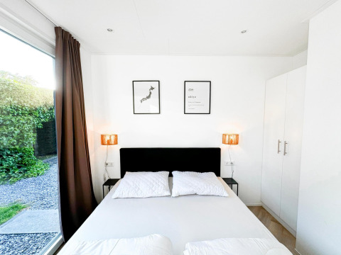 Dormitorio moderno y luminoso en Eco Lodge, Uniq Leisure, Países Bajos, con cama doble y ventanal al jardín.