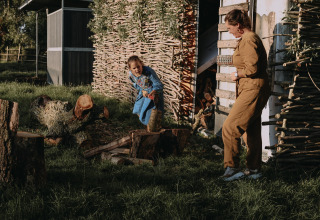 Une femme et une enfant coupent du bois devant une cabane rustique à Feather Down Landgoed ter Wijnendale, Belgique.