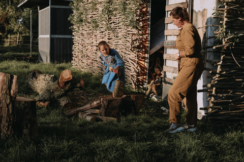 Une femme et une enfant coupent du bois devant une cabane rustique à Feather Down Landgoed ter Wijnendale, Belgique.