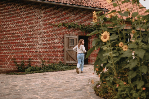 Een meisje wandelt langs de binnenplaats met zonnebloemen bij Feather Down Landgoed ter Wijnendale, West-Vlaanderen.