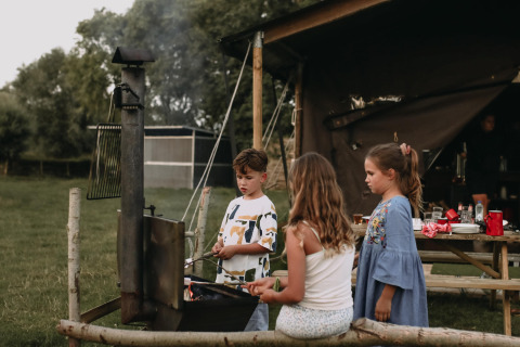 Niños reunidos alrededor de una fogata frente a una tienda en Feather Down Landgoed ter Wijnendale, Bélgica.