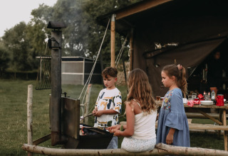 Kinderen zitten rond een kampvuur bij een tent op Feather Down Landgoed ter Wijnendale, België.