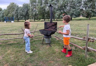 Two children play by an outdoor stove in a grassy park at Feather Down Landgoed ter Wijnendale, Belgium.