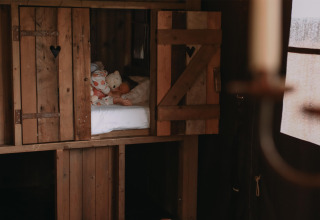 Kindje slaapt met knuffels in een knusse houten hut bij Feather Down Landgoed ter Wijnendale.