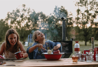 Two smiling children enjoy an outdoor meal at a wooden table at Feather Down Landgoed ter Wijnendale.
