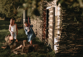 Twee kinderen zijn hout aan het hakken naast een hut op Feather Down Landgoed ter Wijnendale vakantiepark.