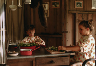 Due bambini in pigiama a fantasia tagliano verdure in una cucina rustica a Feather Down Landgoed ter Wijnendale.