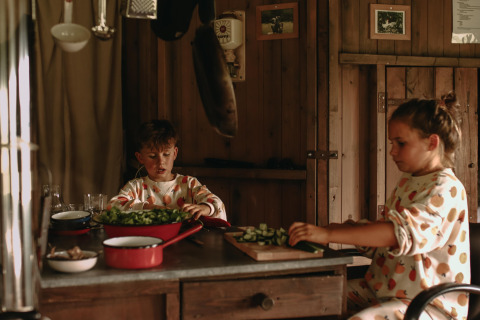 Dos niños con pijamas estampados cortan verduras en una cocina rústica en Feather Down Landgoed ter Wijnendale.