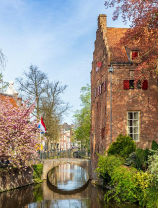 Photo d’un canal pittoresque avec pont, vieux bâtiments en briques et arbres fleuris dans un parc de glamping.