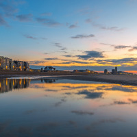 Coucher de soleil sur un parc de vacances en bord de mer offrant des hébergements glamping et reflets d’eau.