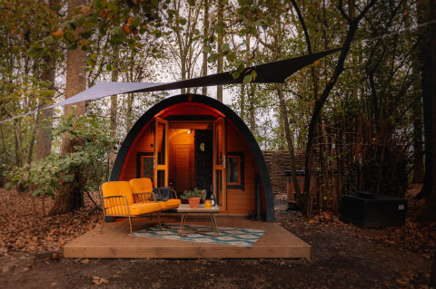 Acogedora tiny house Boshuys con sofá naranja frente a la casa, situada en el bosque de Buitengoed Ruysbos.