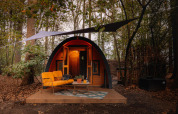 Acogedora tiny house Boshuys con sofá naranja frente a la casa, situada en el bosque de Buitengoed Ruysbos.