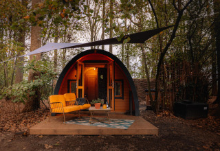 Acogedora tiny house Boshuys con sofá naranja frente a la casa, situada en el bosque de Buitengoed Ruysbos.
