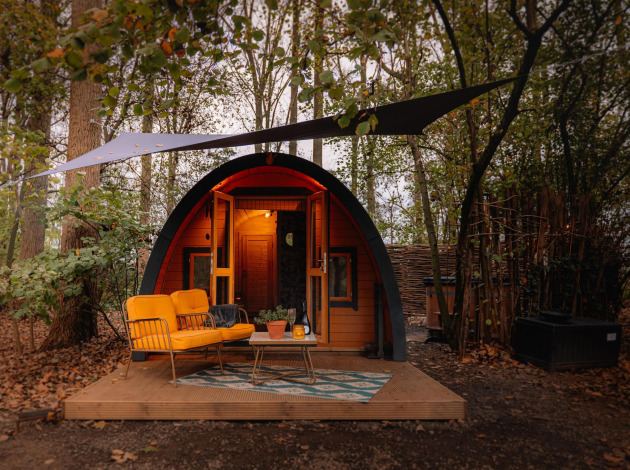 Knus tiny house ‘Boshuys’ met oranje bankje voor de deur, gelegen in het bos bij Buitengoed Ruysbos.