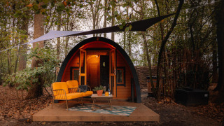 Acogedora tiny house Boshuys con sofá naranja frente a la casa, situada en el bosque de Buitengoed Ruysbos.