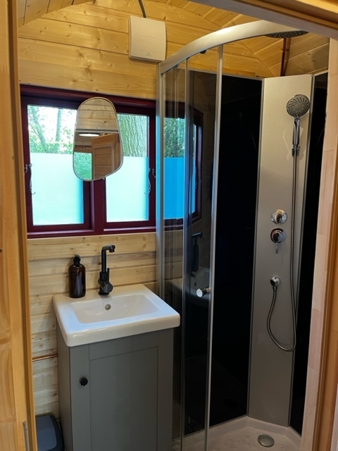 Pequeño baño de madera con ducha curva, lavabo, espejo y ventanas en Boshuys, Buitengoed Ruysbos, Países Bajos.