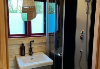 Pequeño baño de madera con ducha curva, lavabo, espejo y ventanas en Boshuys, Buitengoed Ruysbos, Países Bajos.