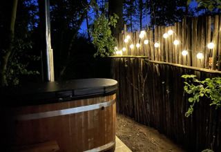 Udendørs spabad med lyskæder ved Boshuys, Buitengoed Ruysbos, Holland, omgivet af træhegn og natur.