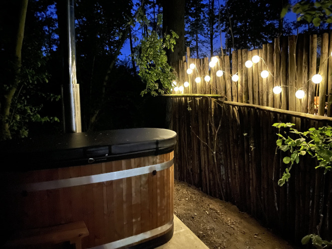 Buitenspa met sfeerverlichting bij Boshuys, Buitengoed Ruysbos, Nederland, omringd door houten schutting.