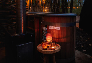 Udendørs badekar og stearinlys på bord ved Boshuys tiny house, Buitengoed Ruysbos, Holland, om aftenen.